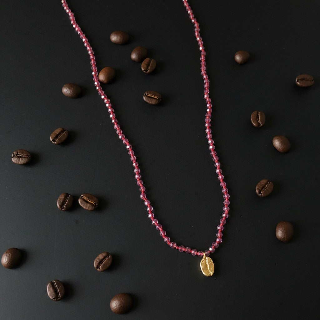 Collana MandalaT Chicco di Caffè con ametiste sfaccettate viola e nodi rossi e ciondolo in bronzo su sfondo nero con chicchi di caffè