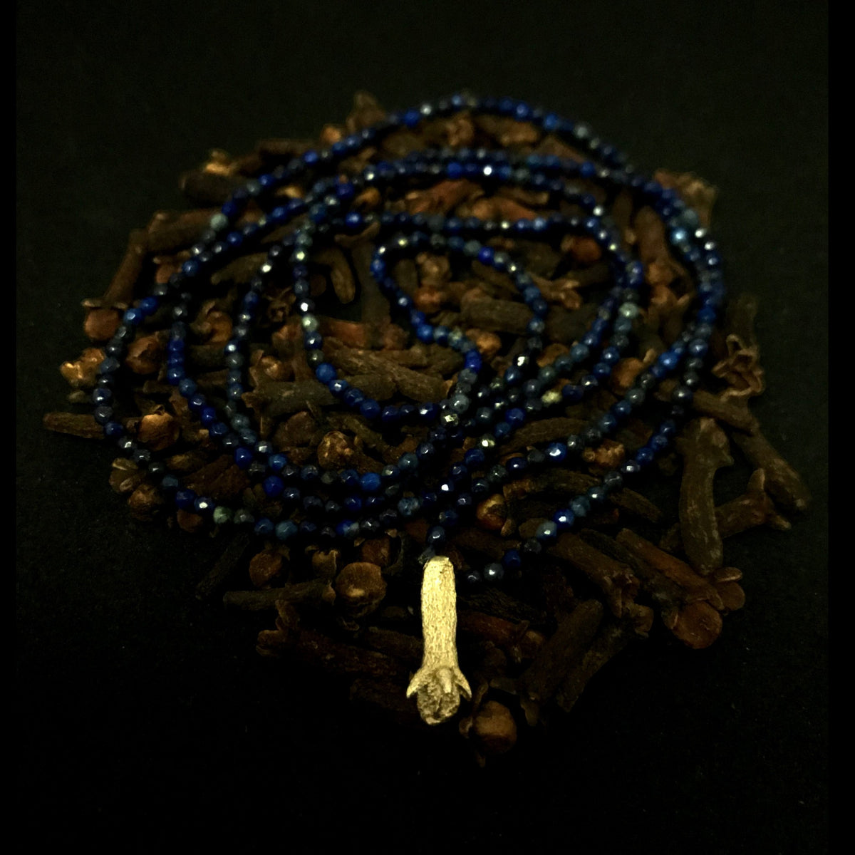 Collana MandalaT con ciondolo a forma di chiodo di garofano in metallo e perline blu scuro su sfondo scuro
