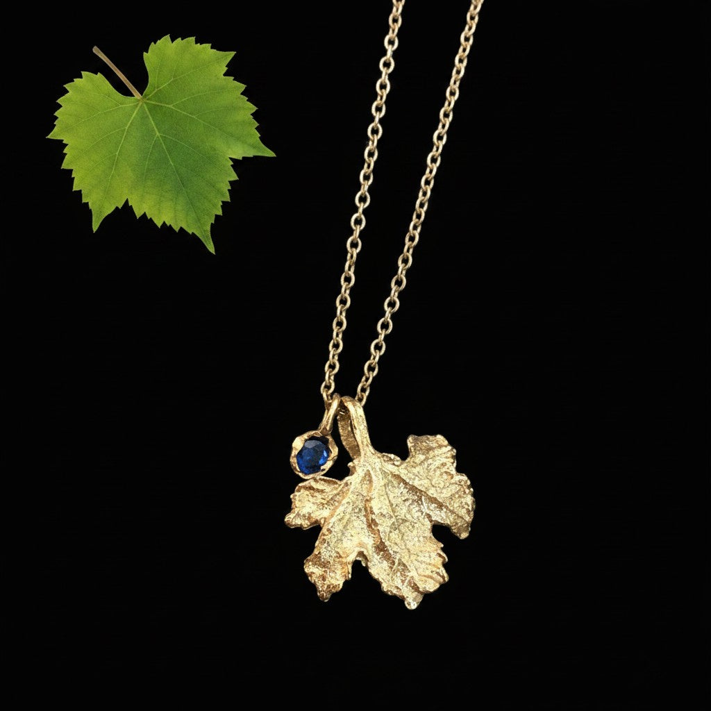 Collana MandalaT in oro con pendente a forma di foglia di vite lavorata e ciondolo Callistemone con zaffiro su sfondo nero