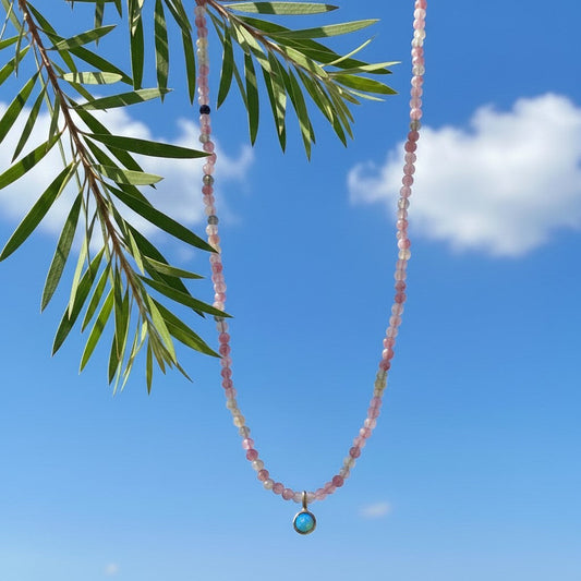 Collana MandalaT Callistemone con Tormaline rosa sfaccettate e ciondolo circolare a forma di Callistemone in oro con Opale azzurro su sfondo di cielo e foglie