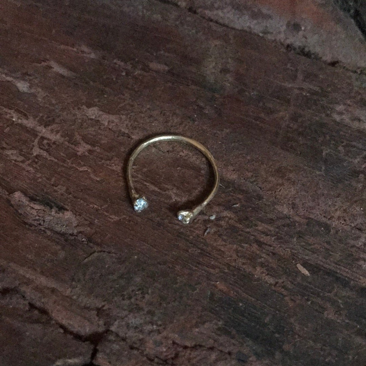 Anello aperto MandalaT Chiodi di garofano in oro con due piccole zirconi luminose su sfondo di legno scuro