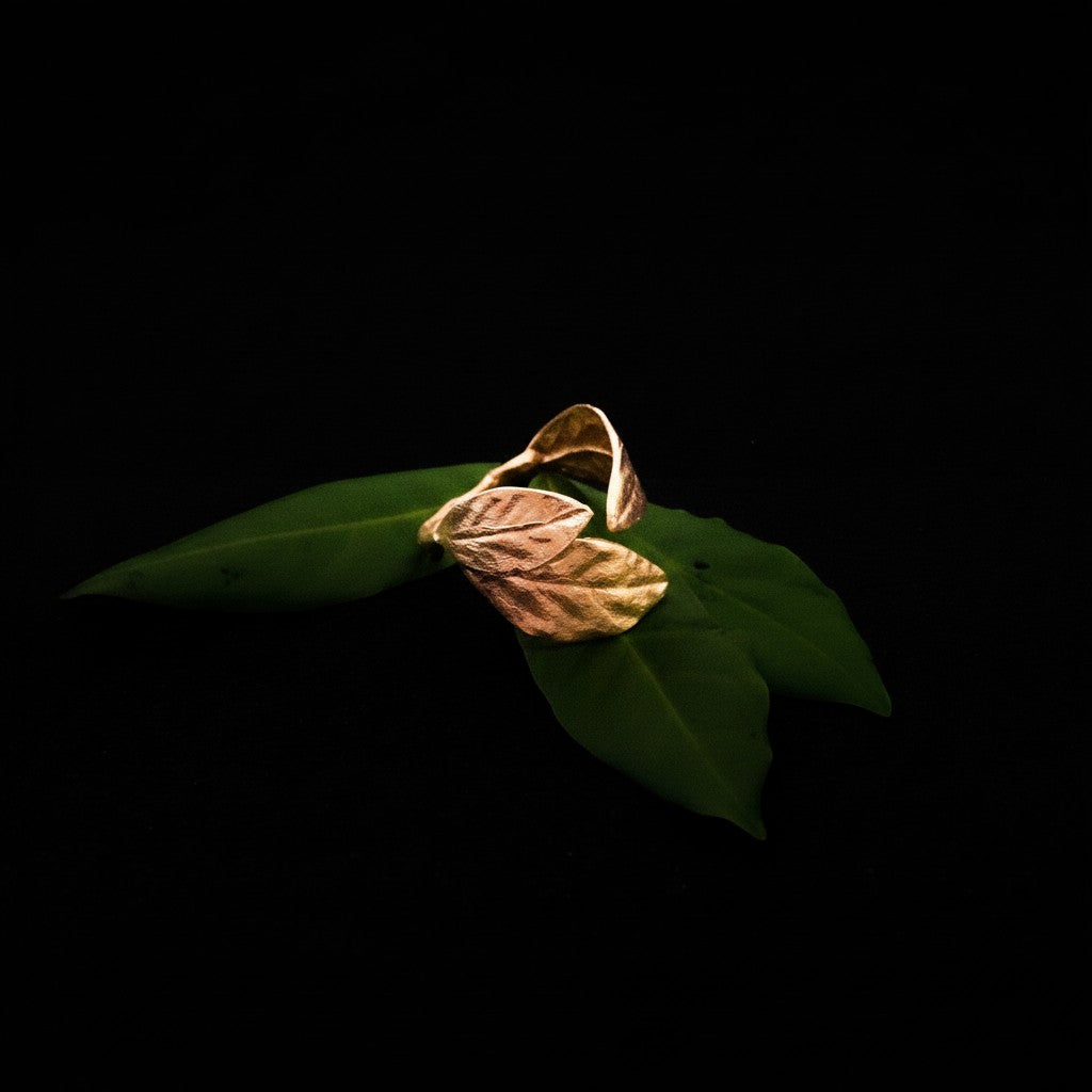 Anello aperto MandalaT in oro rosa con design a foglie di alloro, regolabile e poggiato su foglie verdi
