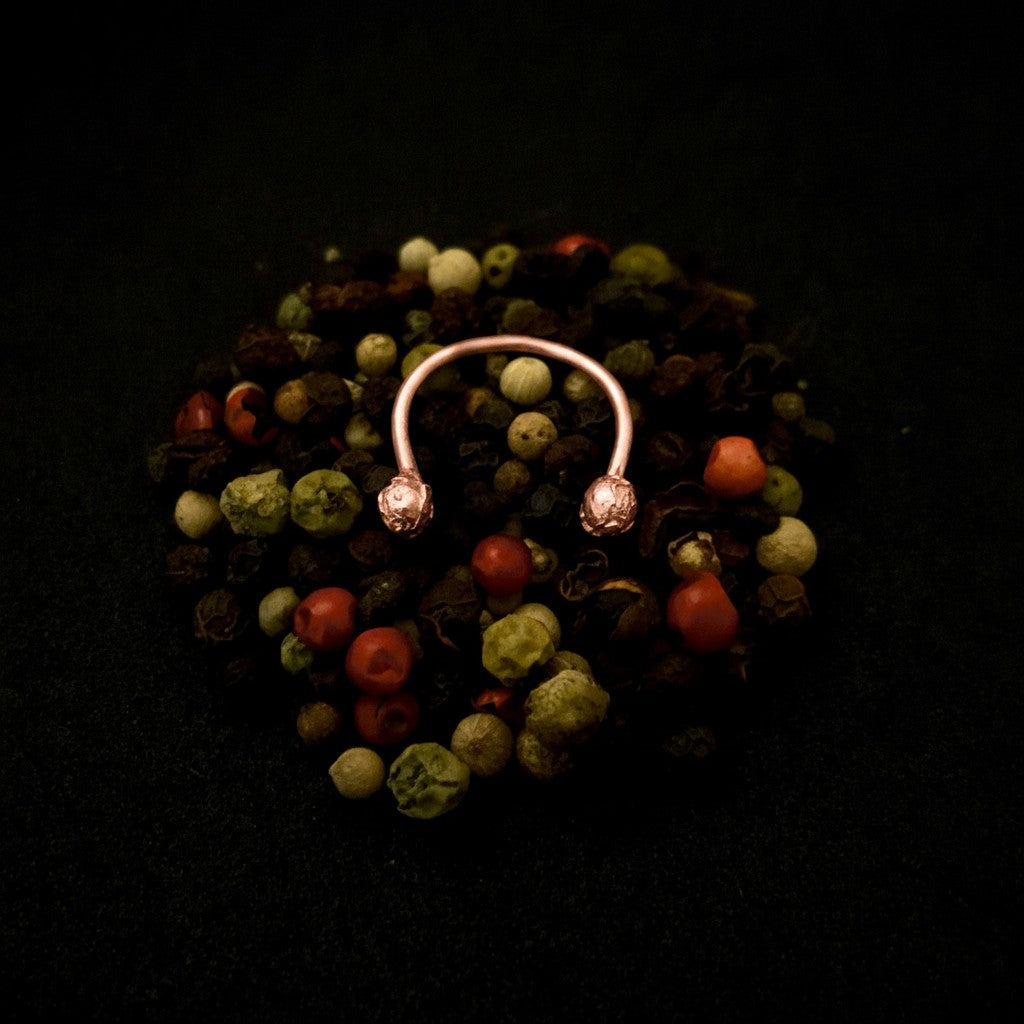 Anello aperto MandalaT in metallo color oro rosa con estremità a forma di granelli di pepe su sfondo scuro
