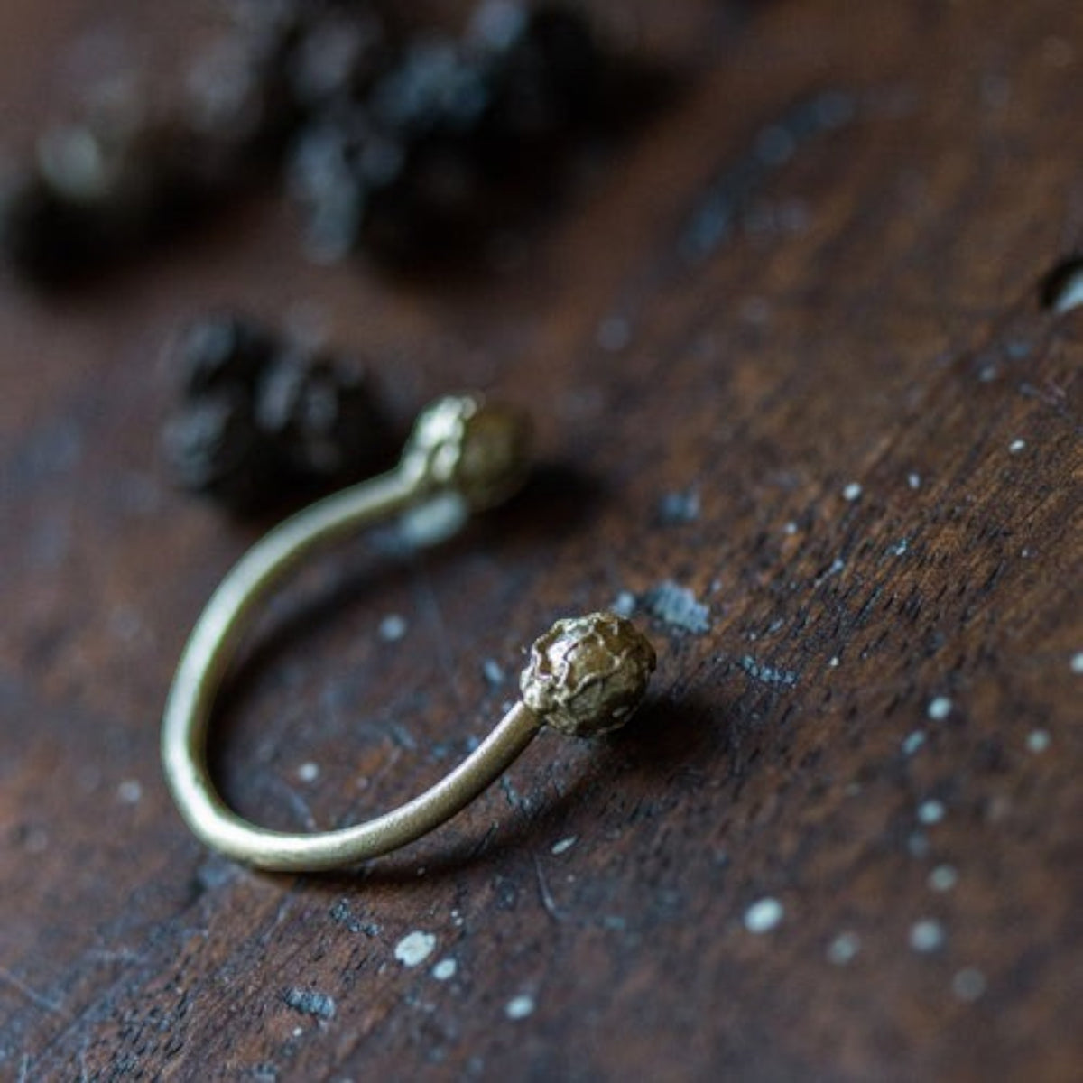 Anello aperto MandalaT in oro con estremità a forma di granelli di pepe su superficie in legno scuro