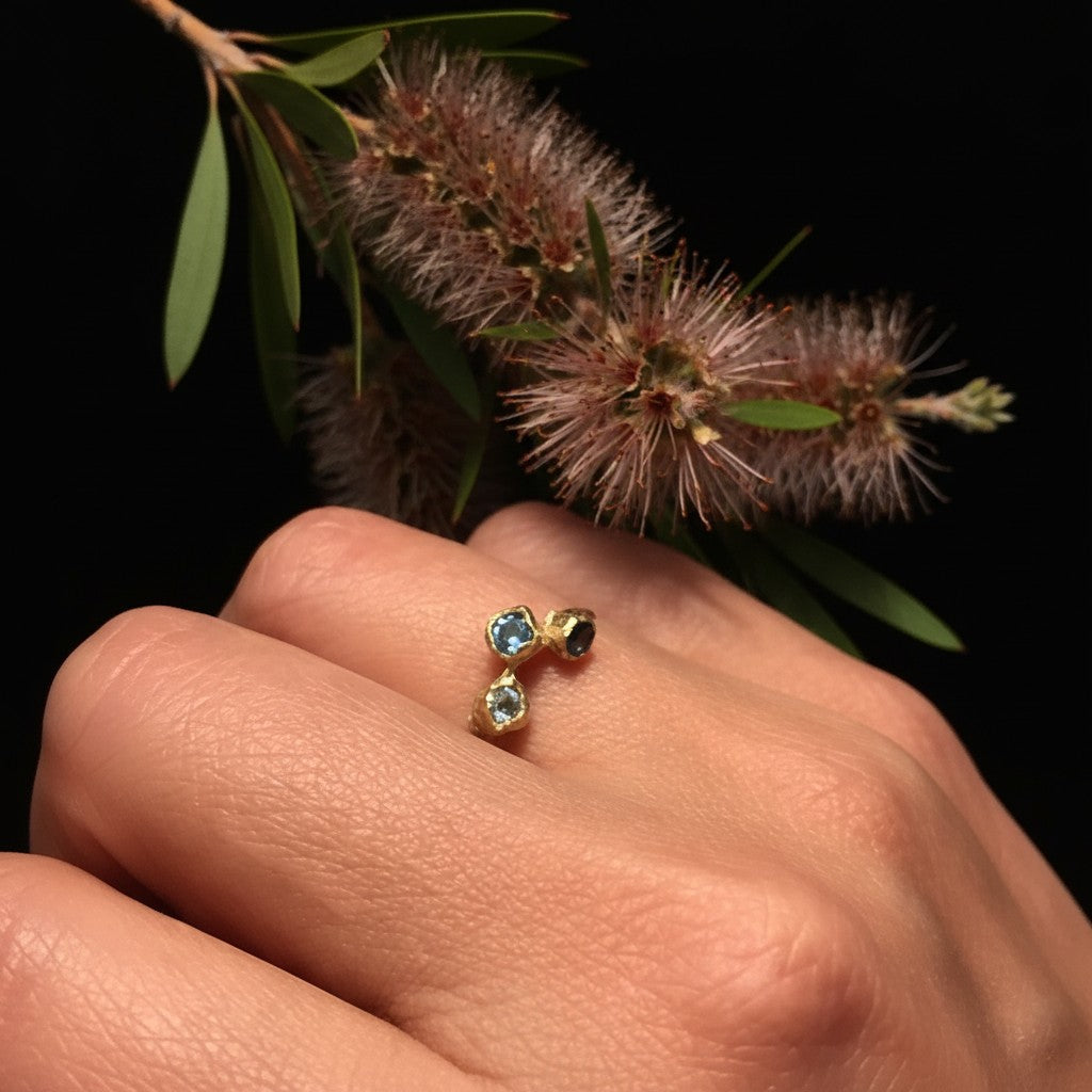 Anello MandalaT Calistemone in oro con Topazi incastonate, indossato su una mano vicino a un fiore