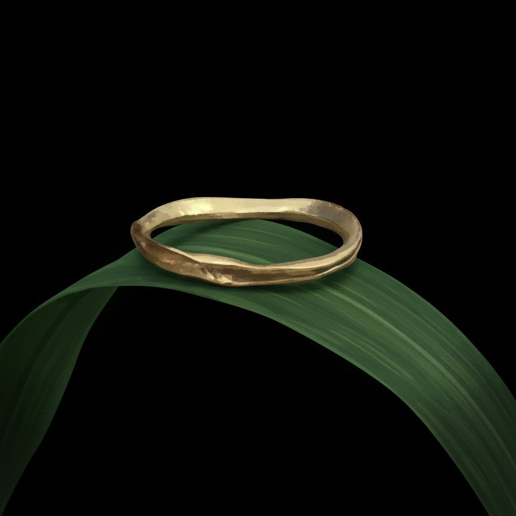 Anello MandalaT filo d'erba in oro dalla forma organica e irregolare appoggiato su una foglia verde