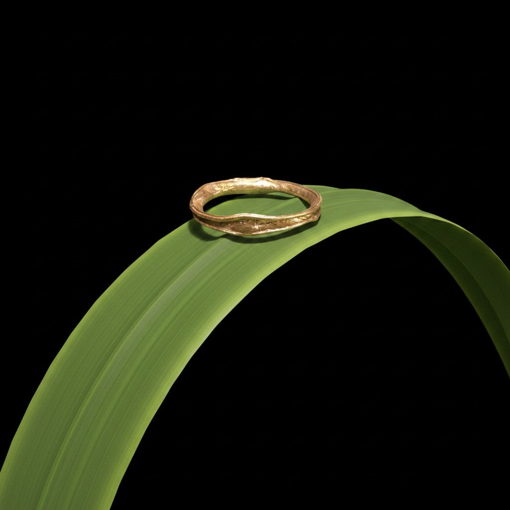 Anello MandalaT filo d'erba in oro con texture organica irregolare poggiato su una foglia verde