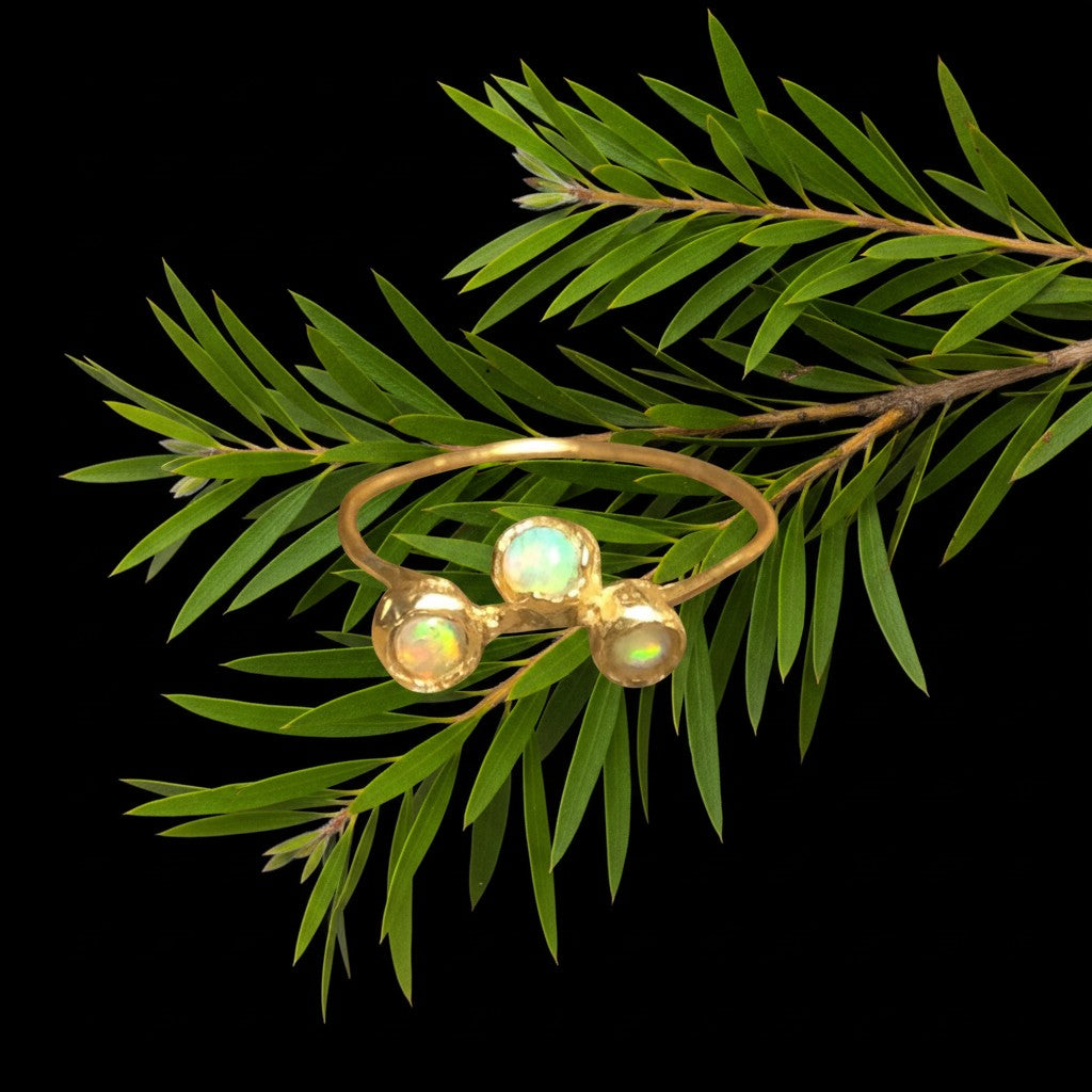 Anello MandalaT Calistemone in oro con tre opali incastonate, poggiato su un ramo di callistemone