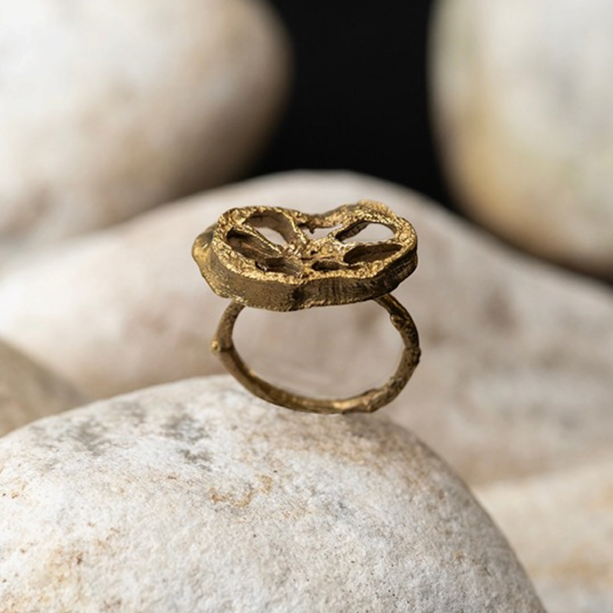 Anello MandalaT Radice di Loto in metallo dorato con texture materica organica poggiato su pietre bianche
