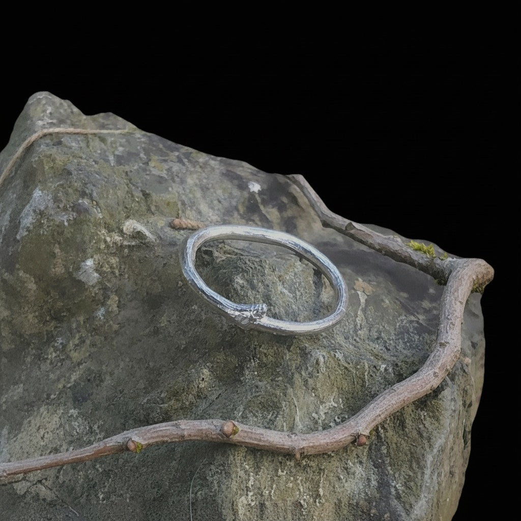 Anello MandalaT a forma di ramo in argento con piccola gemma incastonata, poggiato su una roccia naturale