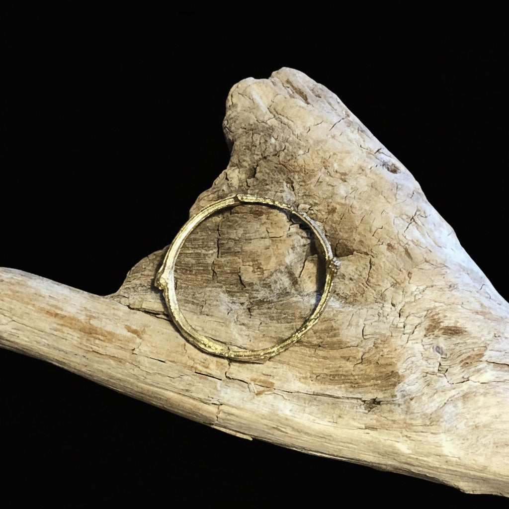 Anello MandalaT a forma di ramo dorato con texture naturale, appoggiato su un pezzo di legno levigato