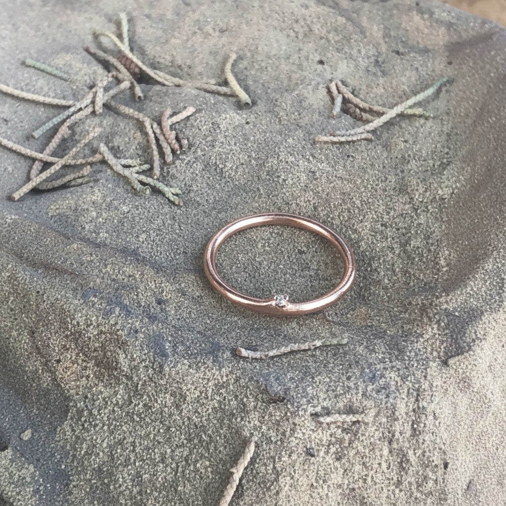 Anello MandalaT a forma di ramo in oro rosa con piccolo diamante incastonato, appoggiato su una superficie rocciosa