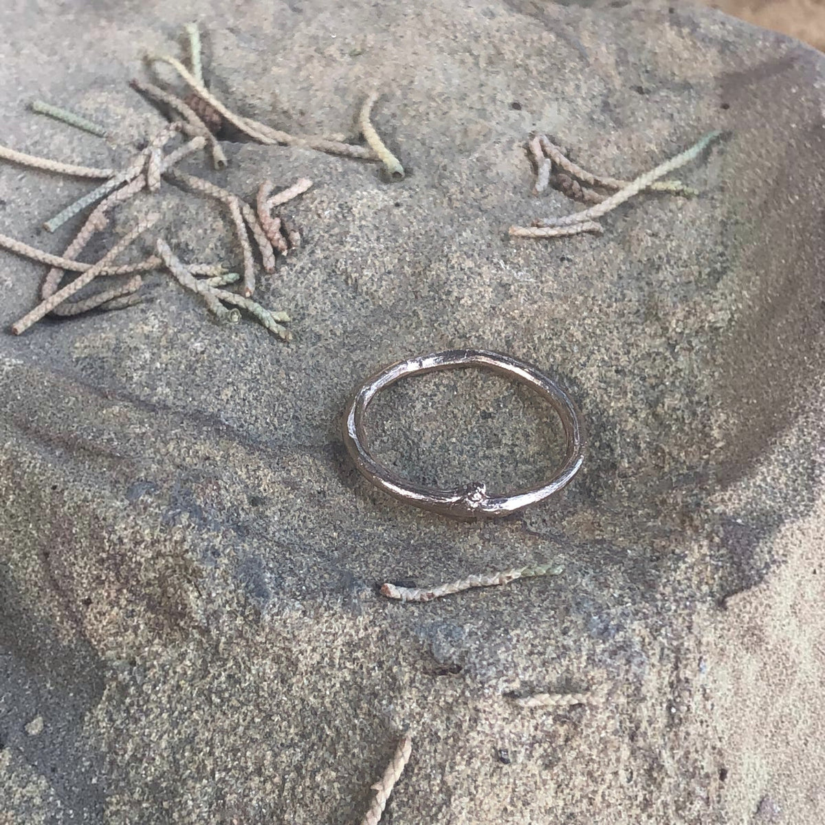 Anello MandalaT a forma di ramo in oro rosa con una piccola gemma incastonata, poggiato su una superficie rocciosa.