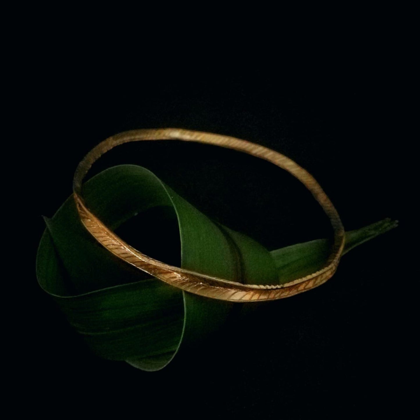 Bracciale MandalaT Filo d'erba in bronzo con texture incisa, poggiato su una foglia verde su sfondo nero