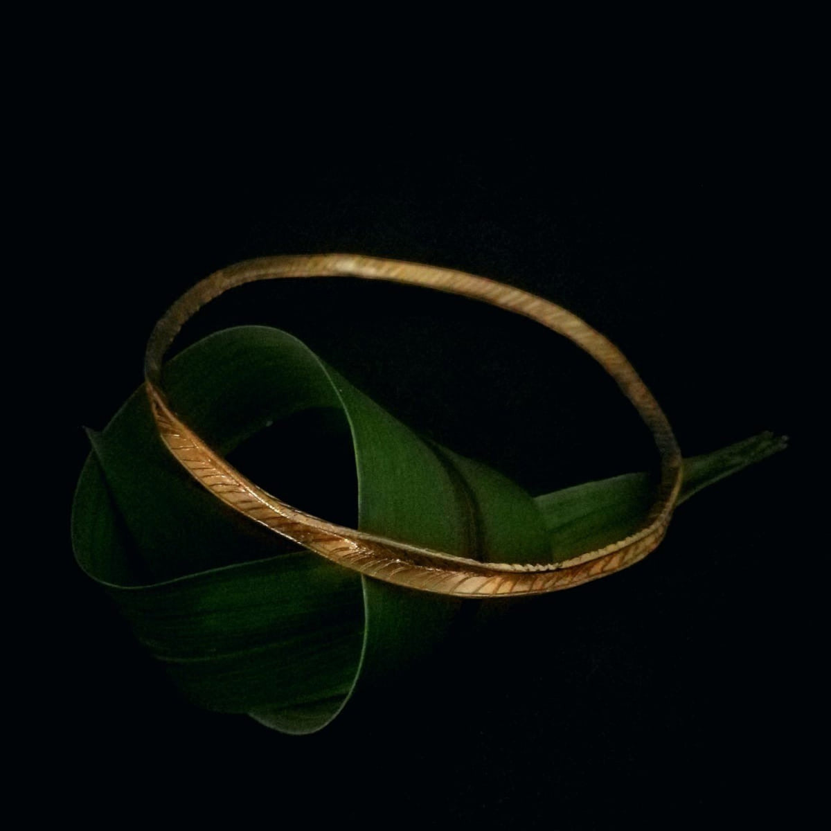 Bracciale MandalaT Filo d'erba in bronzo con texture incisa, poggiato su una foglia verde su sfondo nero