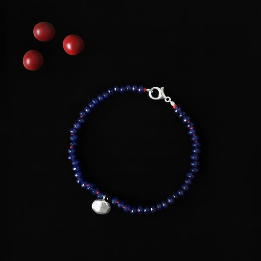 Bracciale MandalaT Ratan Gunja con perle di vetro blu, dettagli in argento e semi rossi su sfondo nero