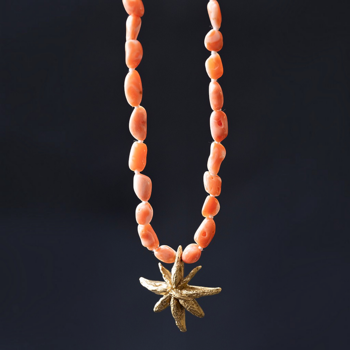 Collana MandalaT con pietre naturali color corallo e ciondolo dorato a forma di anice stellato su sfondo scuro