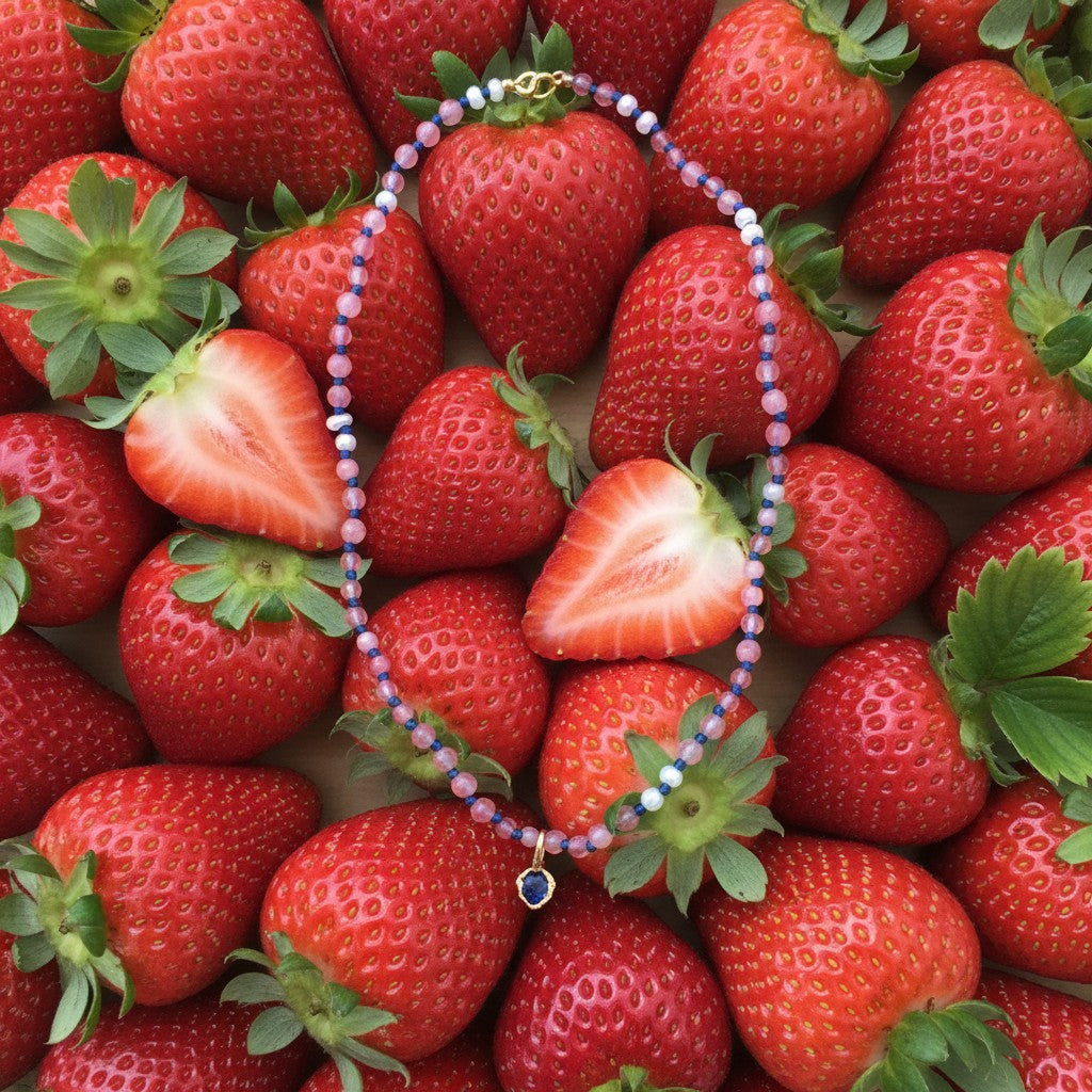 Collana MandalaT Callistemone con pietre rosa e blu e ciondolo a forma di cuore su sfondo di fragole fresche