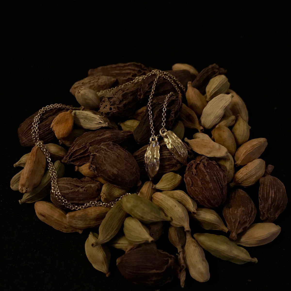 Collana MandalaT in oro con ciondoli a forma di baccello di cardamomo su un letto di Cardamomo