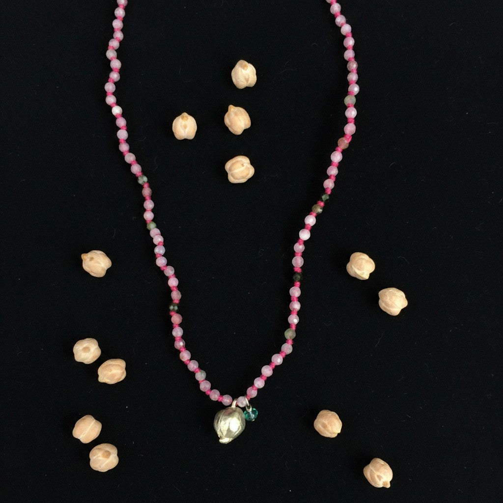 Collana MandalaT Cecio con perline rosa sfaccettate e ciondolo a forma di cece su sfondo nero con ceci veri