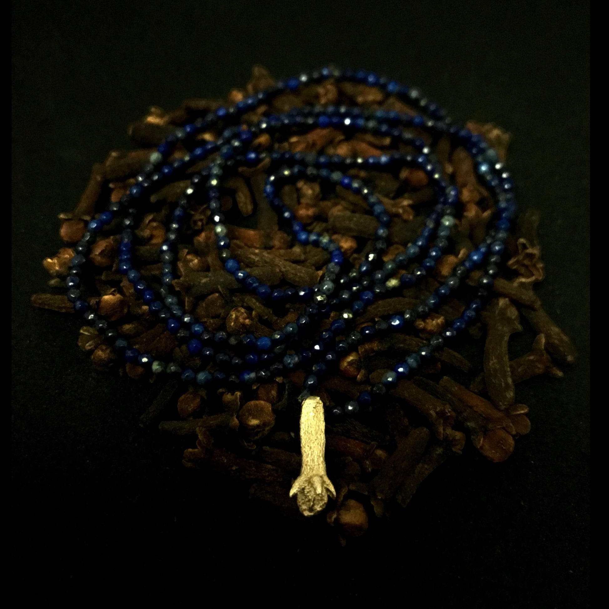 Collana MandalaT con ciondolo a forma di chiodo di garofano in metallo e perline blu scuro su sfondo scuro