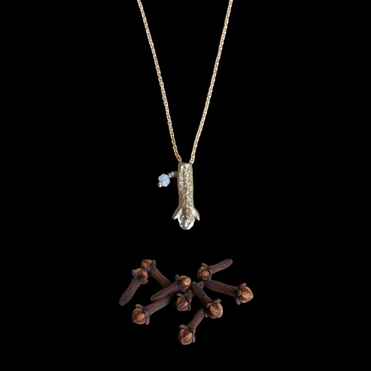Collana MandalaT in oro con ciondolo a forma di chiodo di garofano e piccola pietra azzurra su sfondo nero