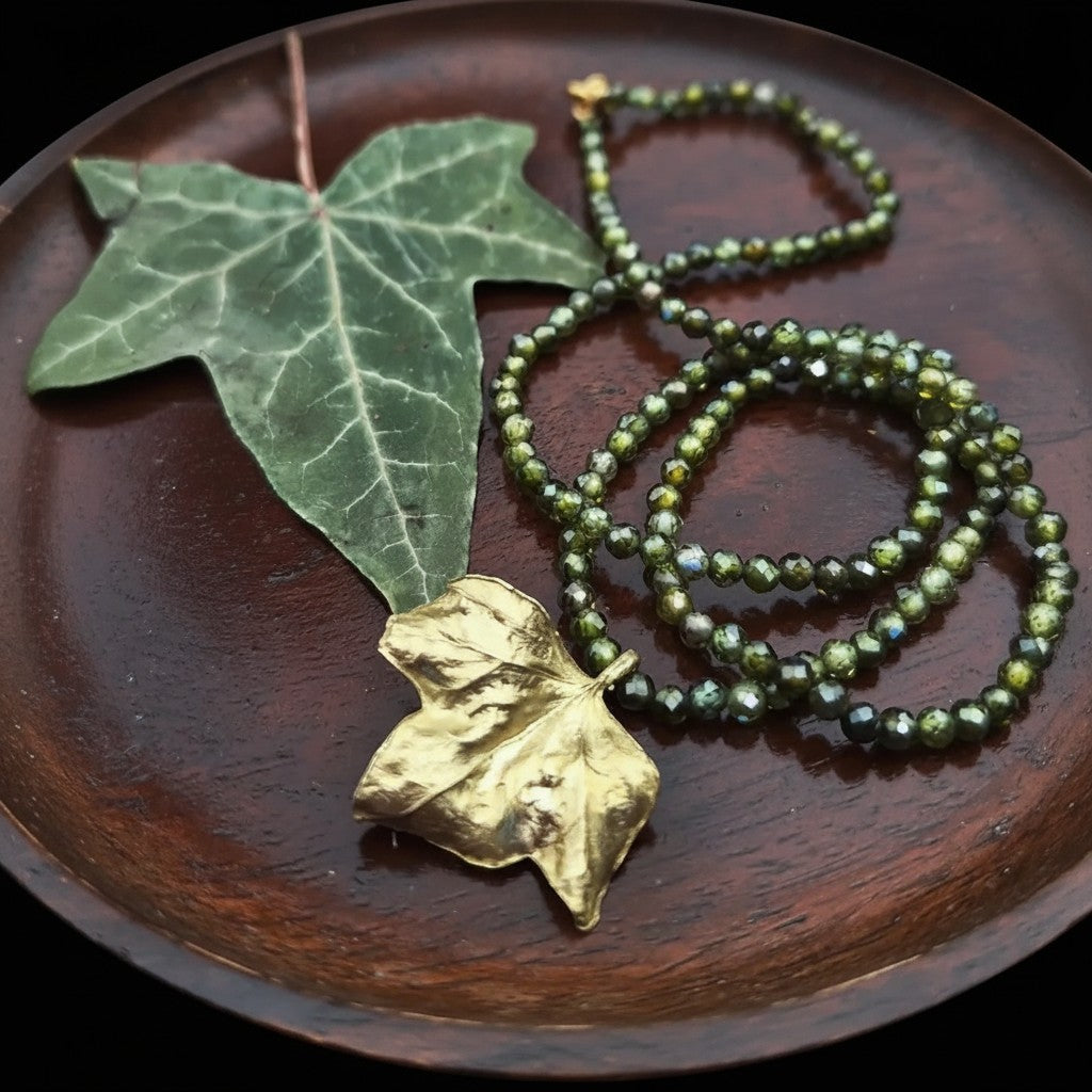 Collana Edera MandalaT con zirconi verdi sfaccettate e ciondolo a forma di foglia dorata su vassoio di legno