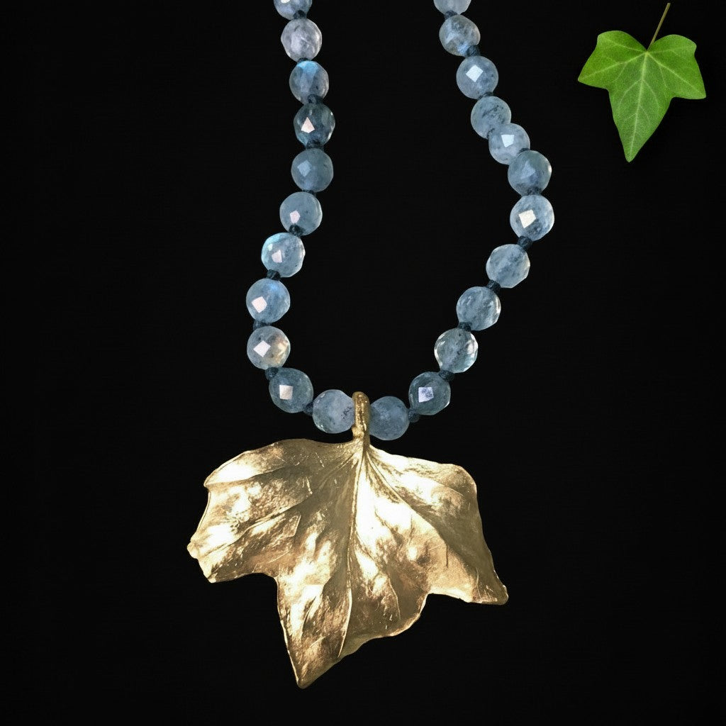 Collana MandalaT Edera con ciondolo a forma di foglia dorata e labradorite sfaccettate azzurre su sfondo nero