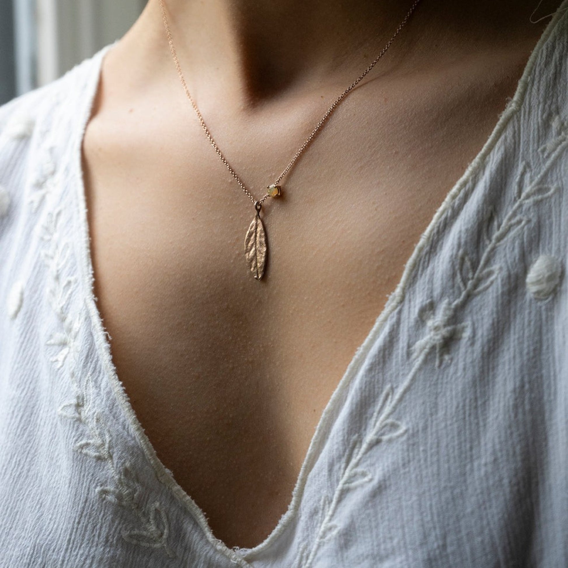 Collana MandalaT in oro rosa con ciondolo a forma di foglia di alloro  e castone con opale welo indossata su camicetta bianca