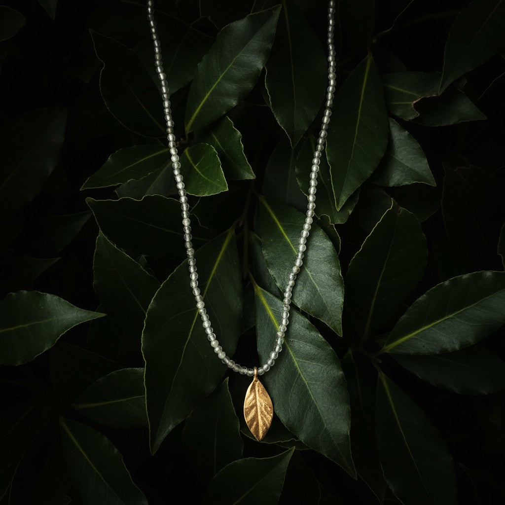 Collana MandalaT con ciondolo a forma di foglia di alloro dorata e catenina di perline di Perite su sfondo di foglie