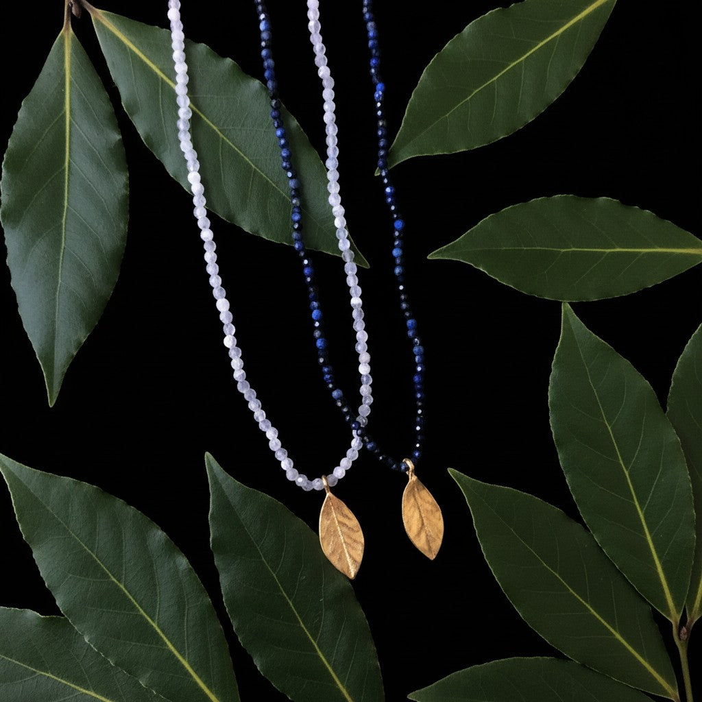 Collana MandalaT con foglia di alloro dorata e pietre dure su sfondo di foglie naturali
