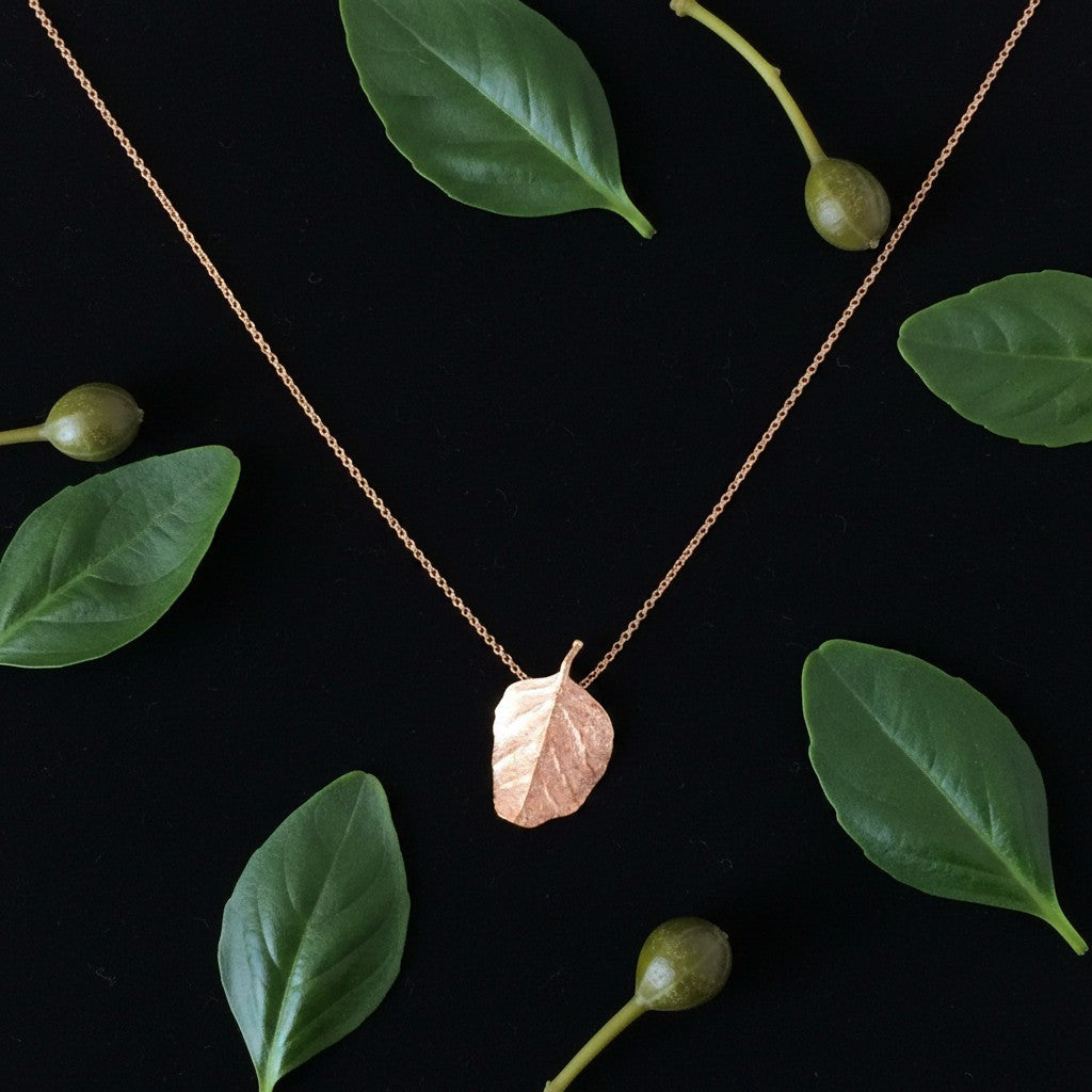 Collana MandalaT in oro rosa con pendente a forma di foglia di cappero, elegante gioiello artigianale su fondo nero.