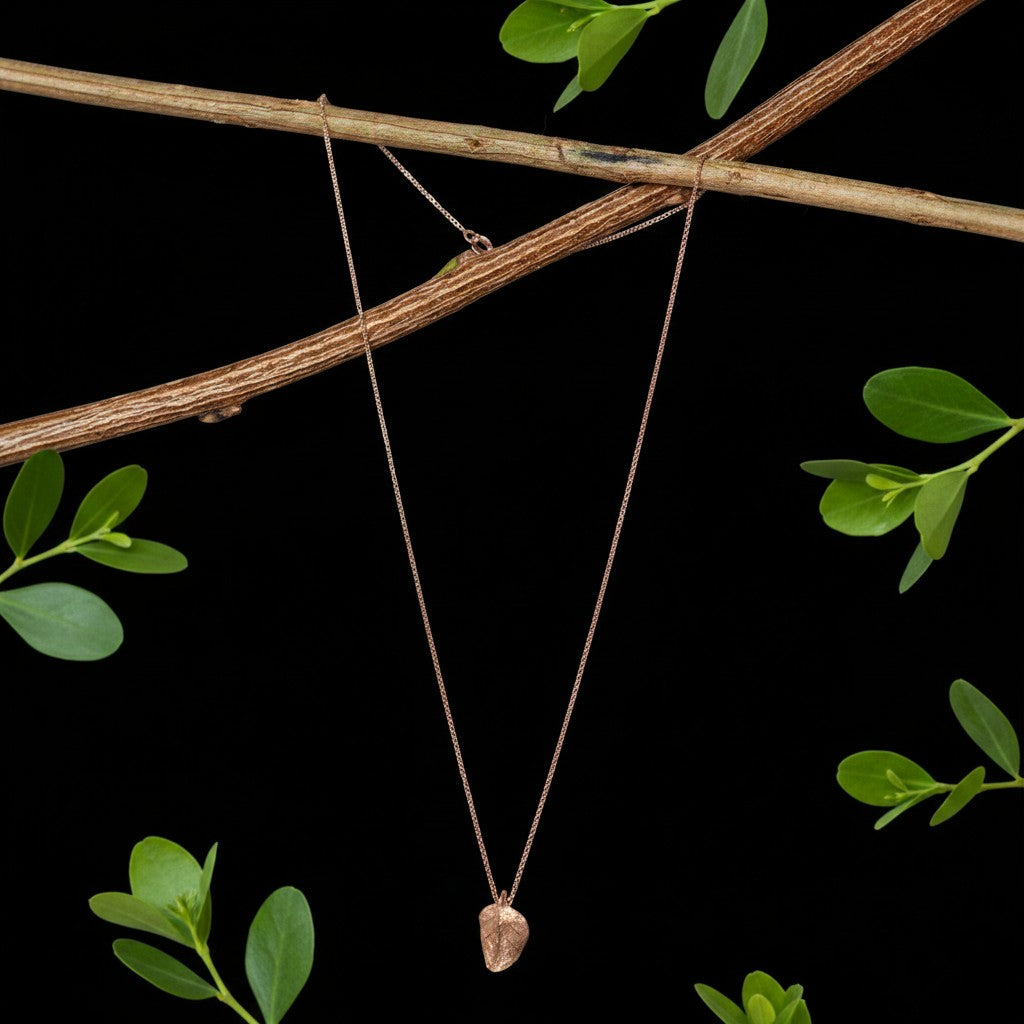 Collana MandalaT in oro rosa con ciondolo a forma di foglia di cappero, appesa a un ramo su sfondo nero