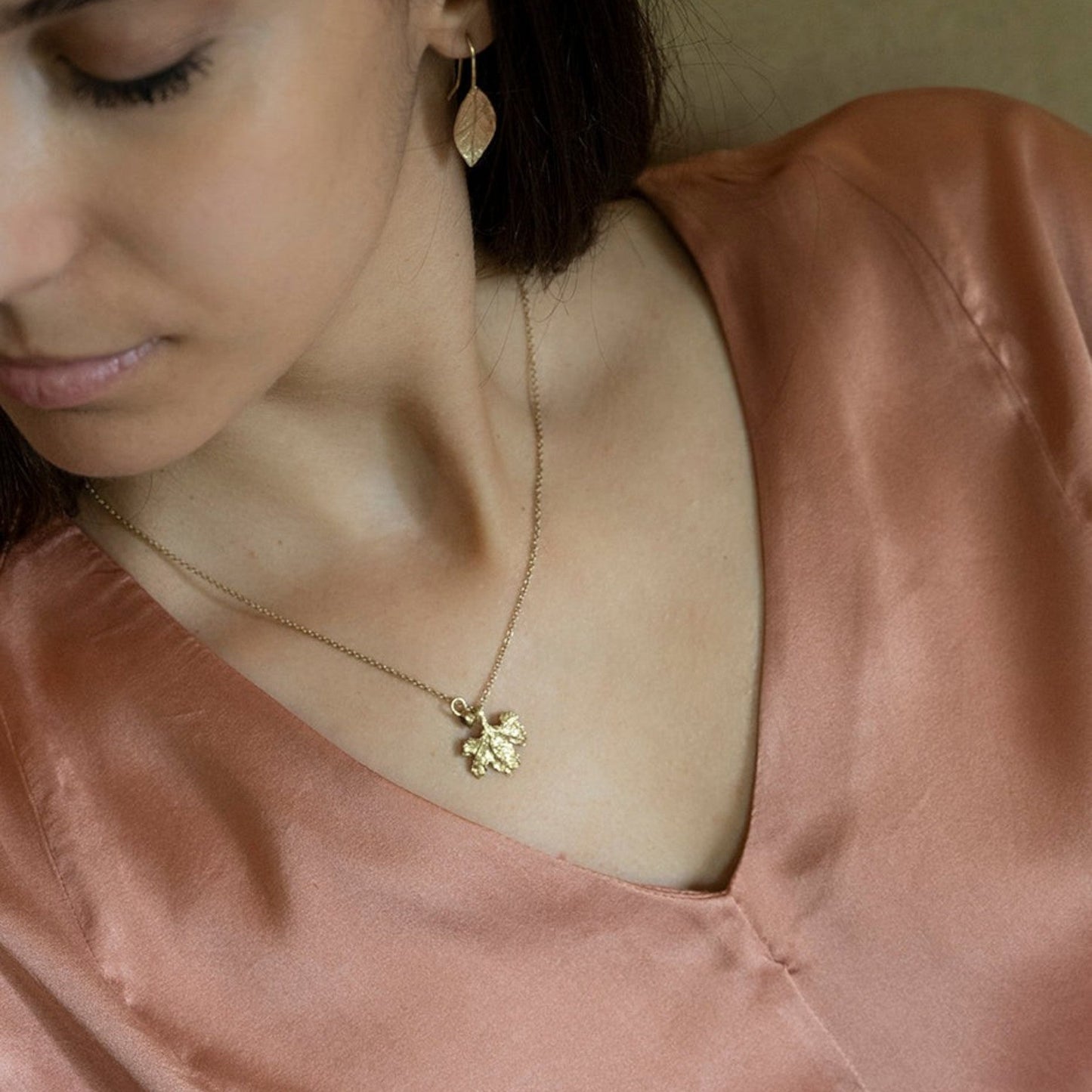 Collana MandalaT con ciondolo a forma di foglia di vite in oro indossata da una donna con orecchini con foglie di alloro
