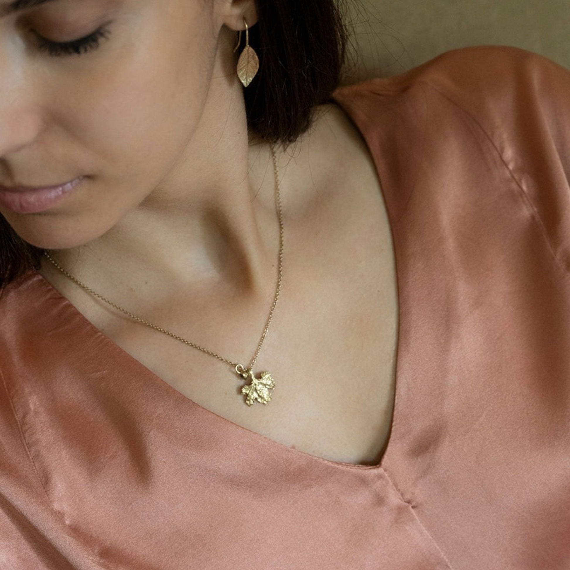 Collana MandalaT con ciondolo a forma di foglia di vite in oro indossata da una donna con orecchini con foglie di alloro