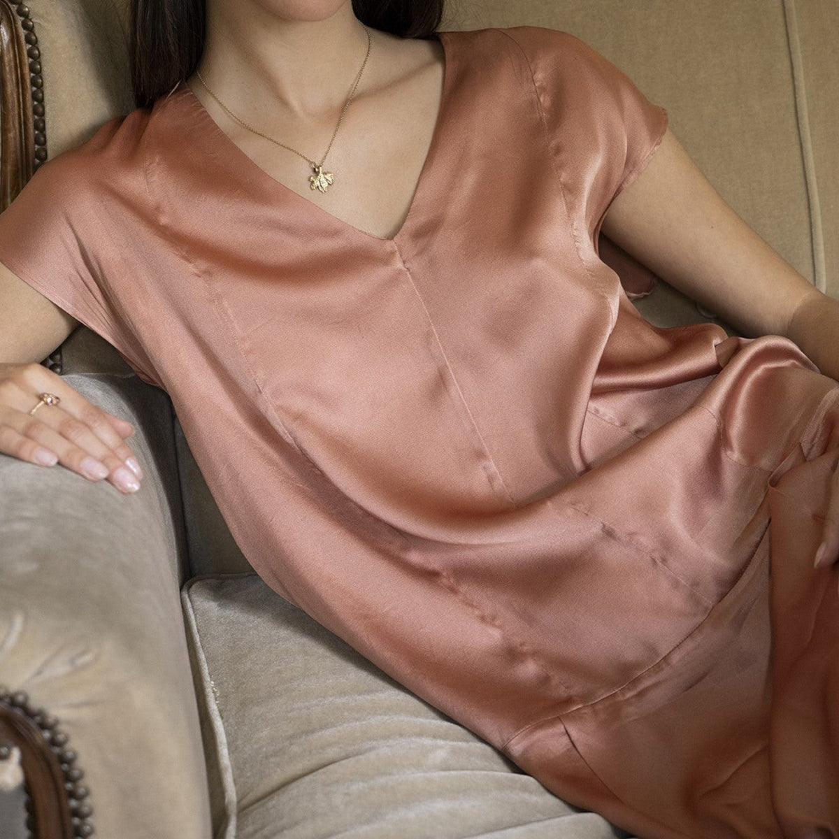 Collana MandalaT con ciondolo a forma di foglia di vite in oro indossata da una donna con abito in seta color pesca