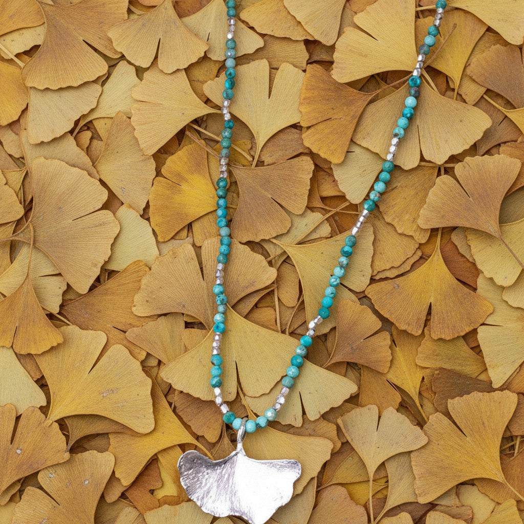 Collana MandalaT con ciondolo a foglia di ginkgo in argento e perline turchesi su letto di foglie autunnali