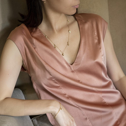 Collana MandalaT Masala in oro con ciondoli a forma di semi e spezie indossata da una donna con vestito in seta rosa