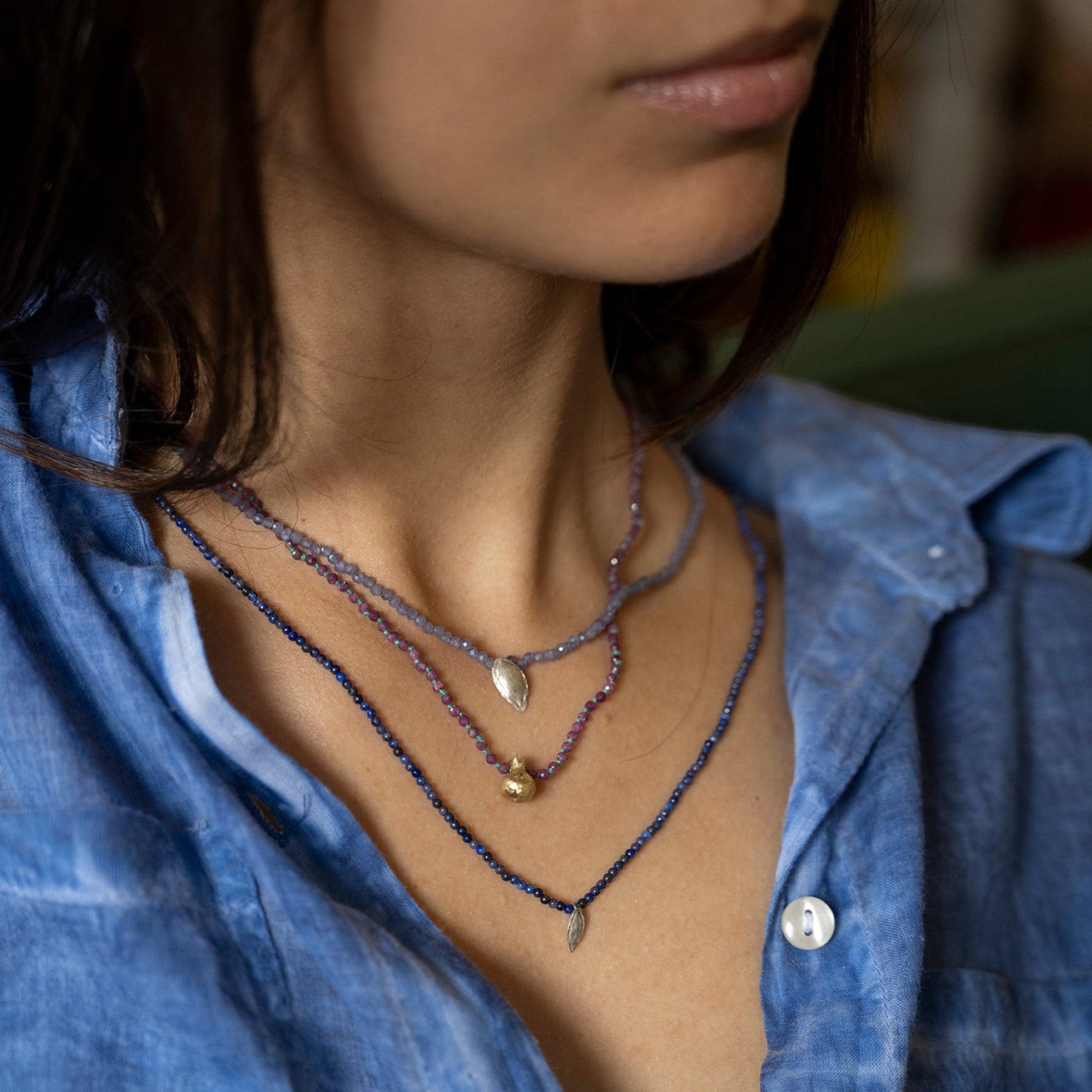 Collana MandalaT con ciondolo melograno e radice di rubino indossata da una donna con camicia azzurra