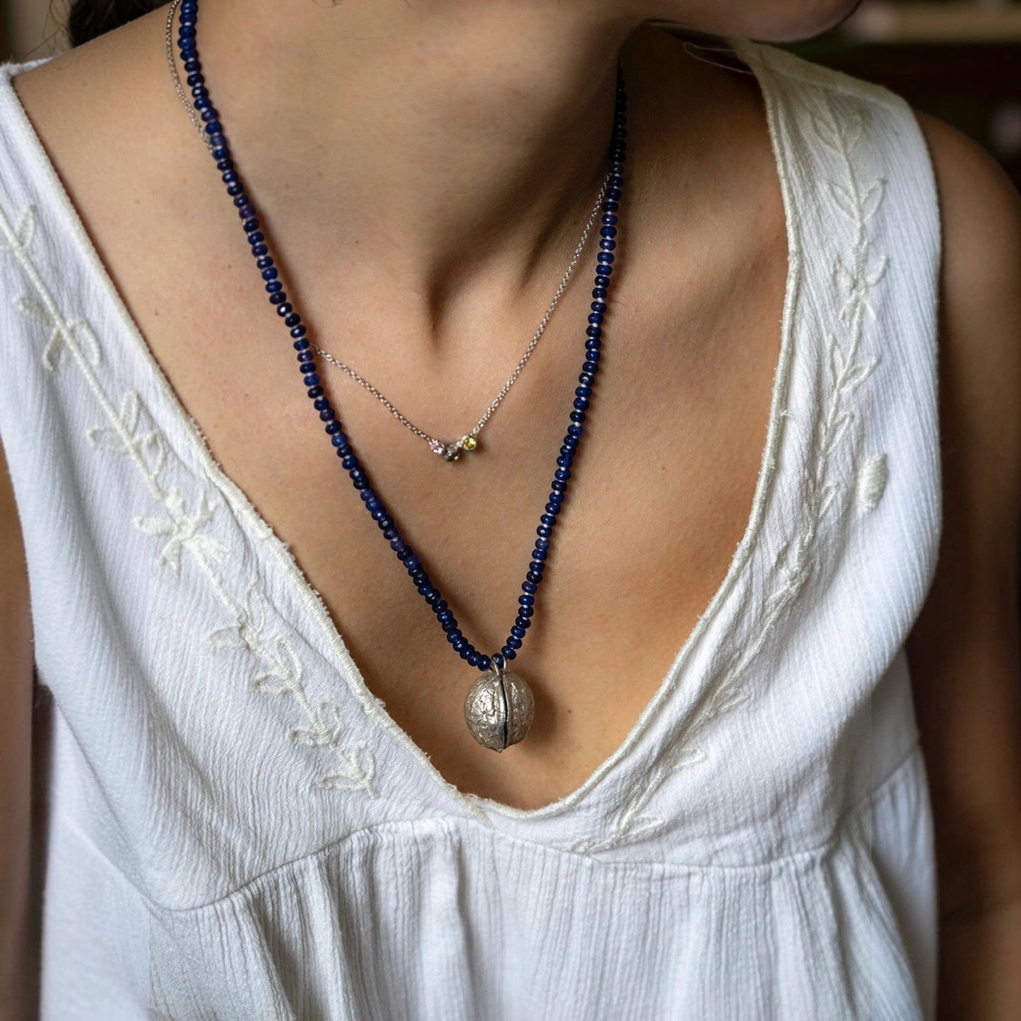 Collana MandalaT con ciondolo a forma di noce in argento su catenina di perline di vetro blu con nodi bianchi indossata da una donna