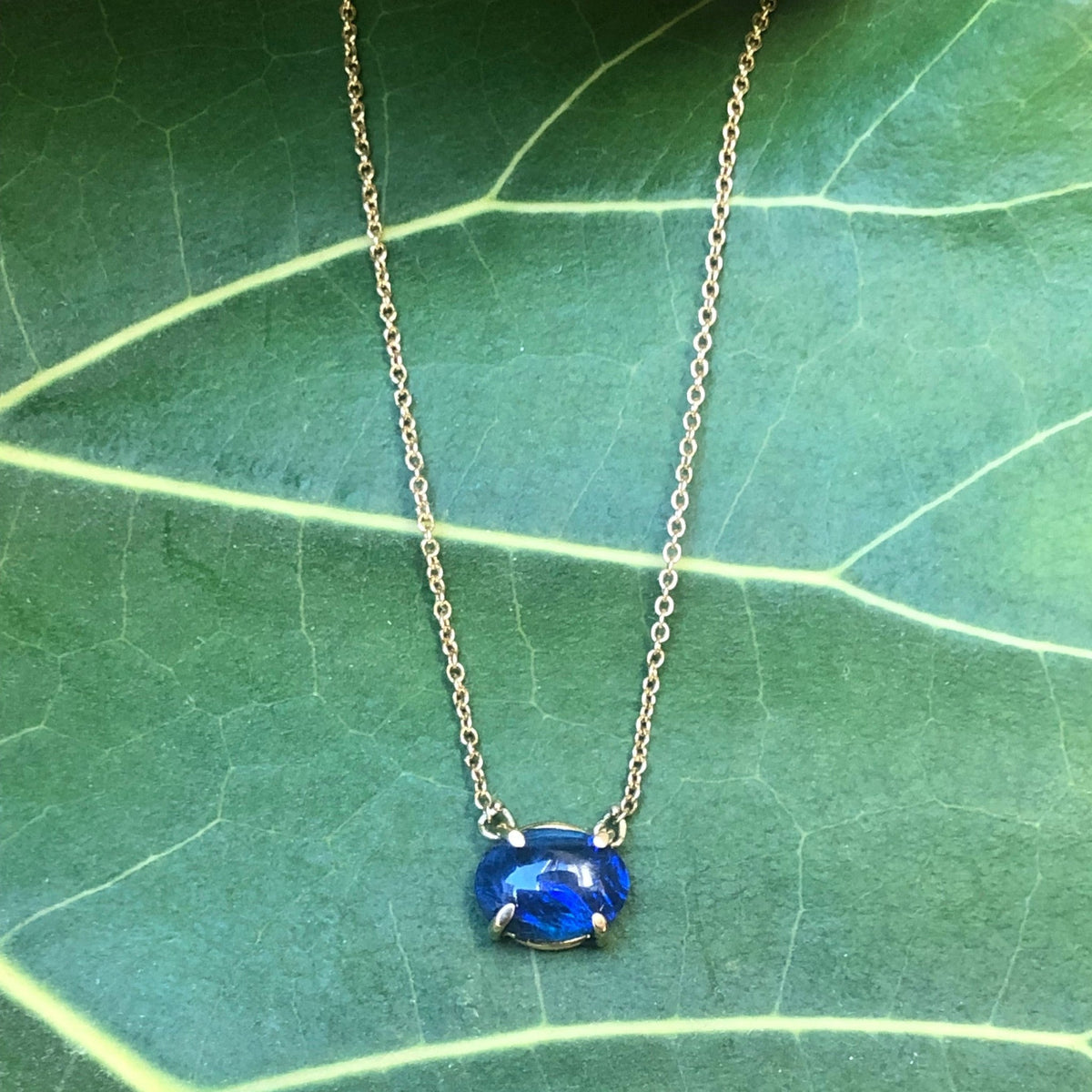 Collana MandalaT con pietra opale blu ovale incastonata in una sottile catenina d'oro su una foglia verde