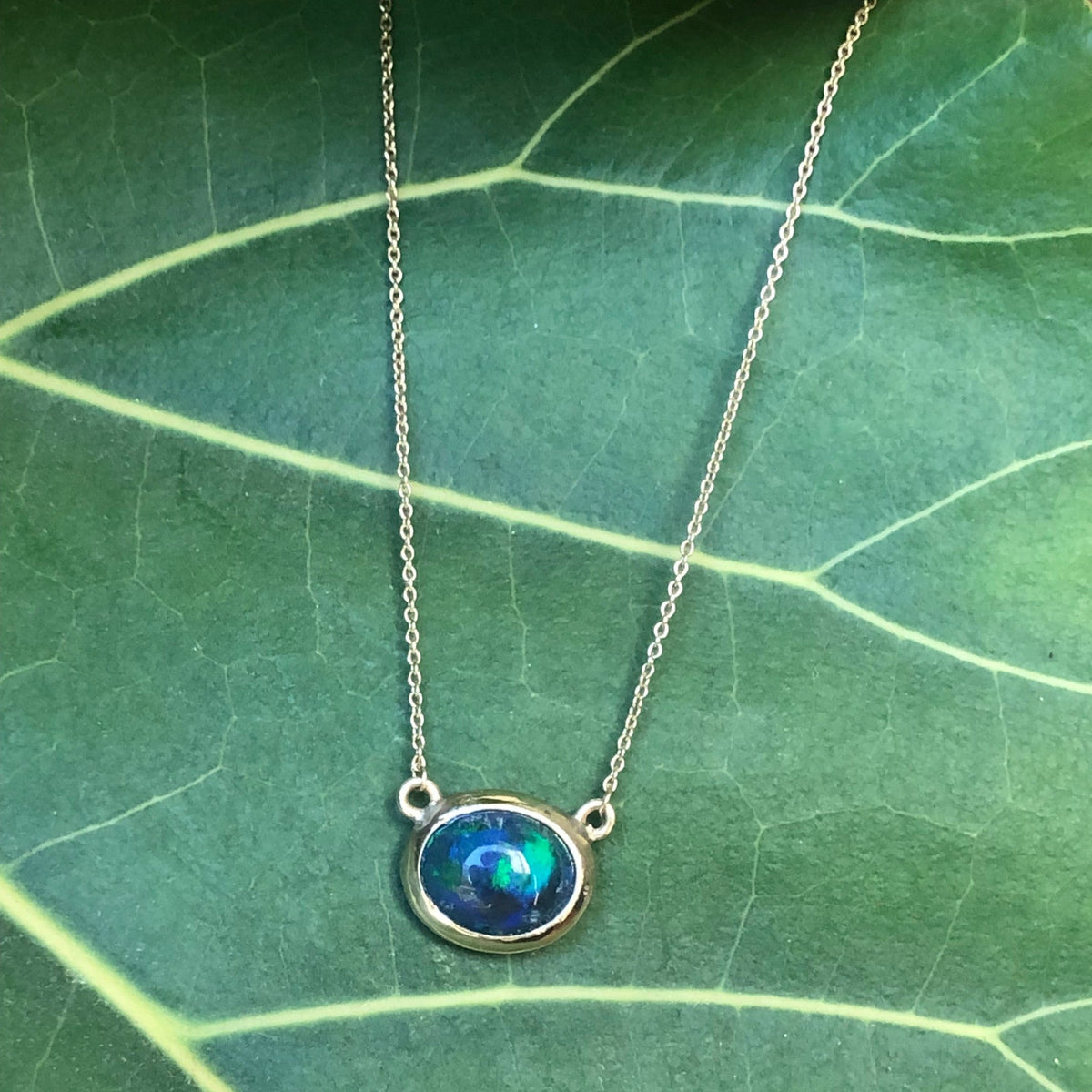 Collana MandalaT con ciondolo in opale blu e verde incastonato in metallo dorato su una foglia verde