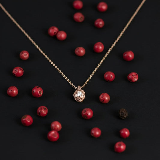Collana MandalaT Pepe in oro con piccolo diamante centrale, circondata da grani di pepe rosa su sfondo nero
