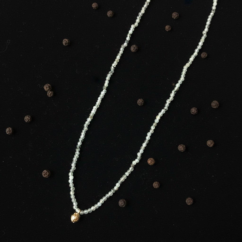 Collana MandalaT Pepe con pietre chiare e ciondolo dorato su sfondo nero con grani di pepe