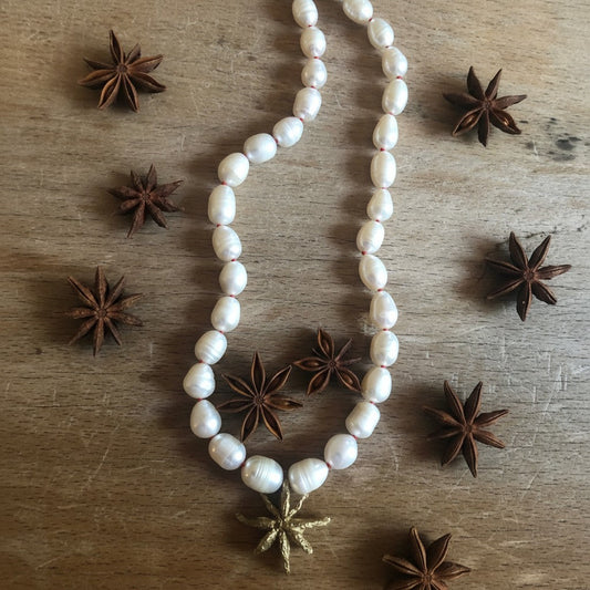 Collana MandalaT Anice Stellata con perle bianche annodate con nodi rossi e ciondolo a forma di anice stellata dorata su fondo in legno