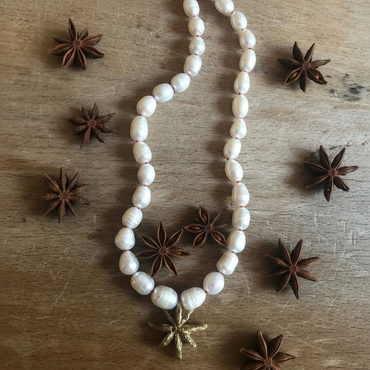 Collana MandalaT Anice Stellata con perle bianche annodate con nodi rossi e ciondolo a forma di anice stellata dorata su fondo in legno