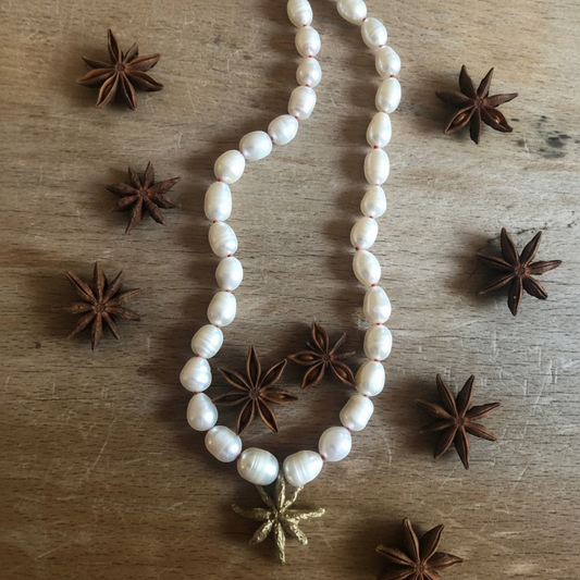 Collana MandalaT Anice Stellata con perle bianche annodate con nodi rossi e ciondolo a forma di anice stellata dorata su fondo in legno