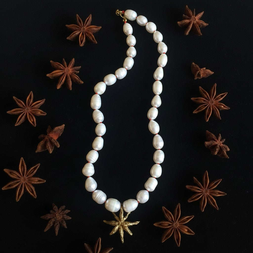 Collana MandalaT con perle barocche bianche annodate con filo rosso e pendente a forma di anice stellata dorata su sfondo nero con anice stellato
