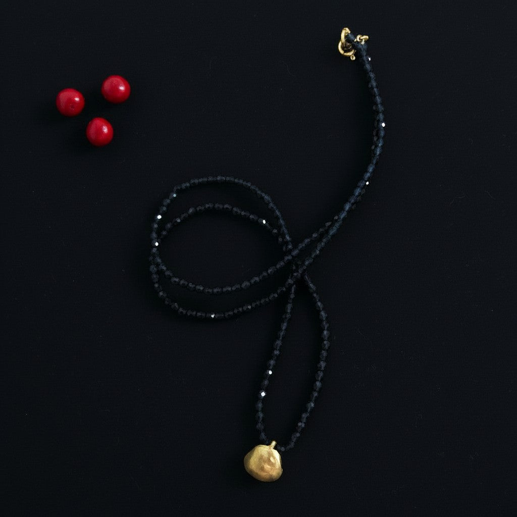 Collana MandalaT con perline di Spinello blu scuro sfaccettate e ciondolo in bronzo, accompagnata da tre semi Ratan gunj rossi