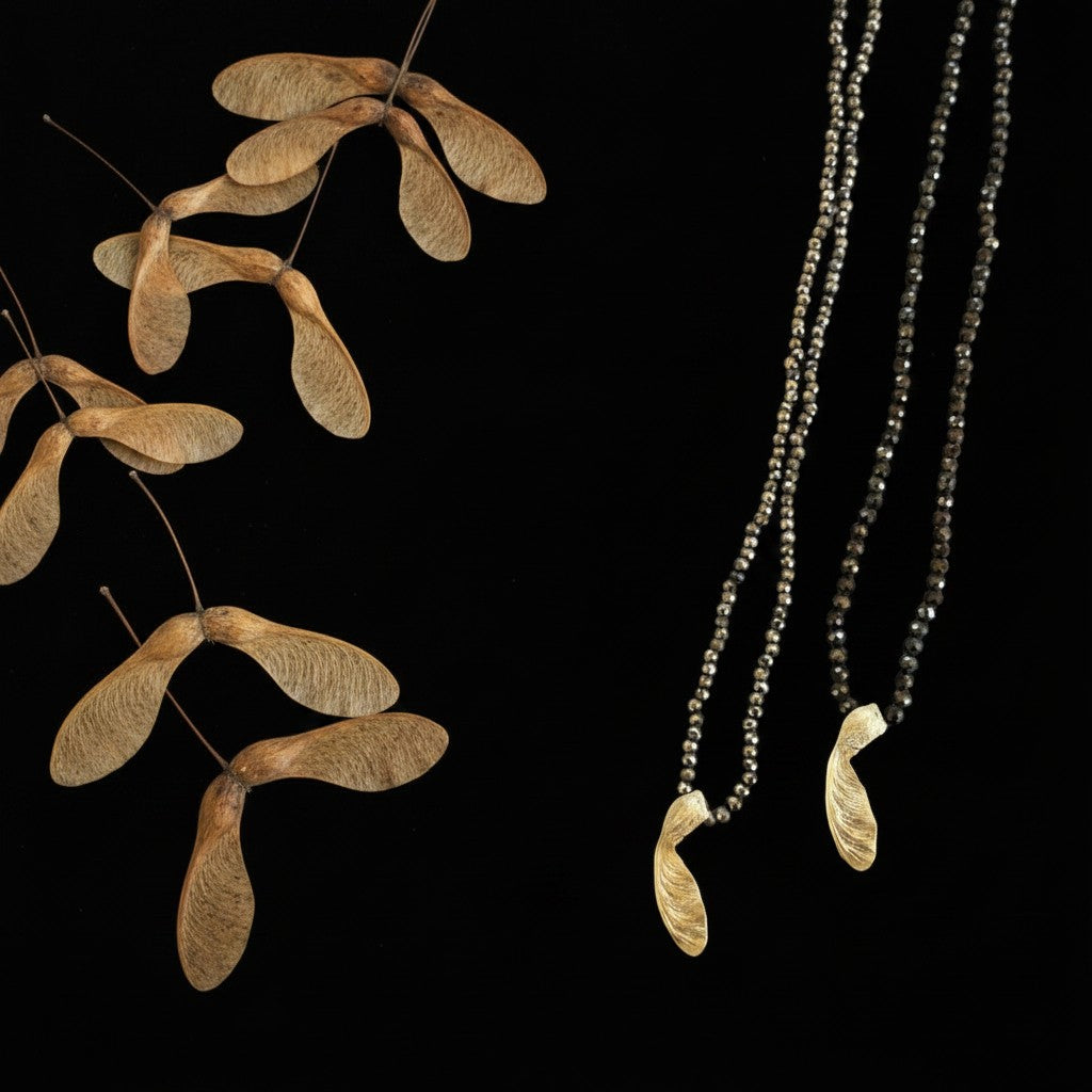 Collana Seme di Acero MandalaT con ciondoli dorati a forma di seme e catenine di perline di Ematite su sfondo nero